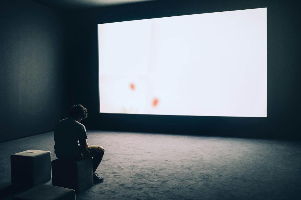 Homme seul assis dans l’obscurité face à un écran vide, illustrant pourquoi tant d’hommes souffrent en silence.