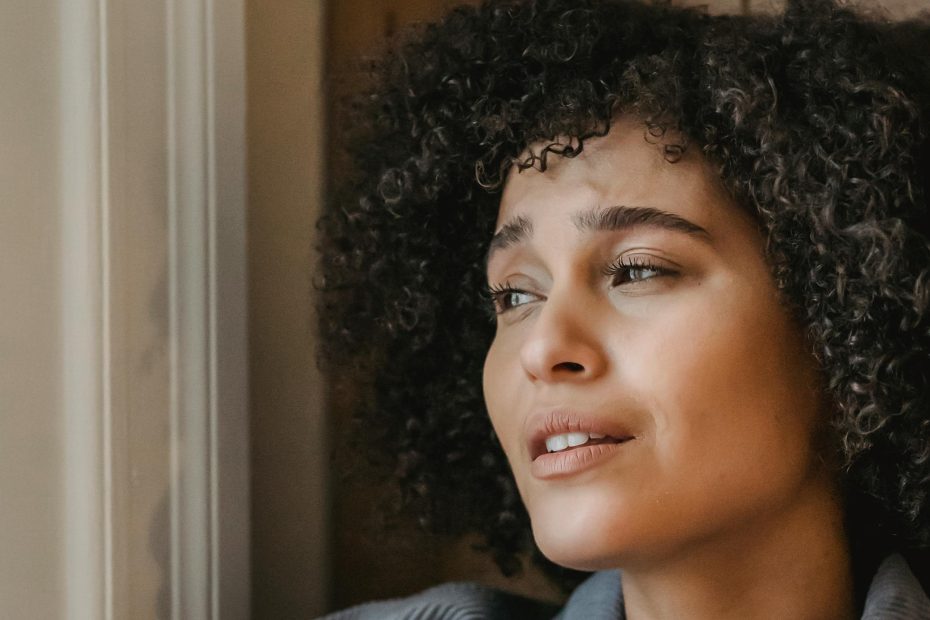 Femme pensive regardant par la fenêtre, exprimant solitude et confusion émotionnelle