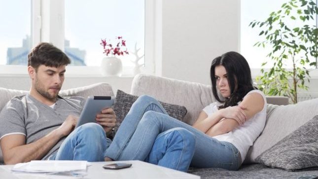 Homme la tête sur sa tablette tandis que sa compagne est triste et déprime suite à des critiques blessantes dites sans cris et sans insultes. Pour illustrer l'emprise émotionnelle et une relation toxique